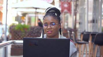 African american woman in street cafe works on her laptop. Back at work with social distance precautions video