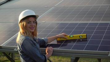 Engineer female inspector in a white helmet check the vertical level of the solar panel by spirit level. The green energy concept video