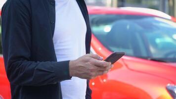 Confident man using smartphone near modern car. Closeup of young businessman using his smartphone video