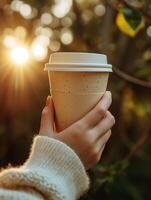 AI generated A close up of a woman's hand clasping a hot coffee cup made from recyclable paper, bathed in the gentle warmth of early morning sunlight photo