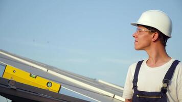 Young enginneer installing new sunny batteries. Worker in a uniform and hardhat installing photovoltaic panels on a solar farm. The future is today. Green energy concept video