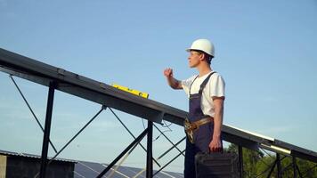 Young enginneer installing new sunny batteries. Worker in a uniform and hardhat installing photovoltaic panels on a solar farm video