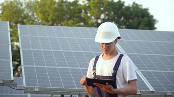 zonne- paneel technicus werken met zonne- panelen. ingenieur in een uniform met een tablet cheques zonne- panelen productiviteit. de toekomst is vandaag video