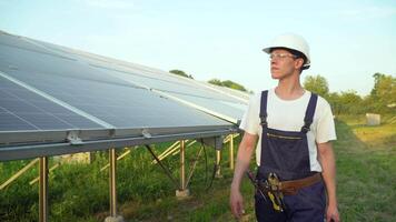 ingenieur wandelen in zonne- cel boerderij door veld- van zonne- panelen controle de panelen Bij zonne- energie installatie. zonne- cellen zullen worden een belangrijk hernieuwbaar energie van de toekomst video