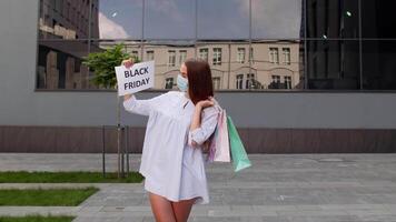 meisje in beschermend masker met boodschappen doen Tassen tonen zwart vrijdag opschrift gedurende coronavirus video