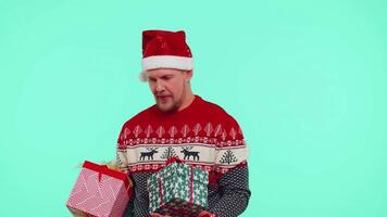 Man wears red New Year presenting Christmas gift boxes, stretches out his hands to camera smiling video