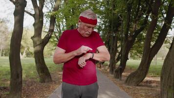 Senior velho homem corrida dentro parque e usando inteligente assistir, rastreamento resultado depois de ginástica exercite-se video