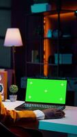 Vertical Video African american young woman looks at laptop with greenscreen, sitting at her home desk and preparing to attend online university lessons. Girl using pc with isolated mockup layout. Camera B.