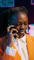 Vertical Video African american student answering call on mobile phone line, talking to her tutor about course materials and lecture notes to use on bachelor paper. Girl exchanging ideas with mentor. Camera A.