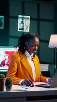 Vertical Video Dedicated woman diligently typing on laptop in the comfort of her home office, writing school essay to finish university homework. African american student working on improving knowledge. Camera B.