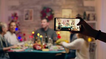 flicka tar foton av henne familj använder sig av smartphone på jul återförening. traditionell festlig jul middag i flera generationer familj. njuter xmas måltid fest i dekorerad rum. stor familj återförening video