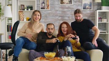 Excited man playing video games and trying to make her friend lose using wireless controller.