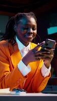 Vertical Video College student doing her homework at laptop and texting on phone, enjoying school break to check social media apps. Girl researching for assignments and using smartphone. Camera B.