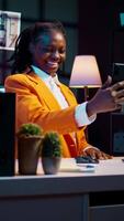 Vertical Video Young woman waving at phone videocall with tutor and classmates, asking for guidance in creating presentations and slideshows. African american student attending online class conference. Camera B.