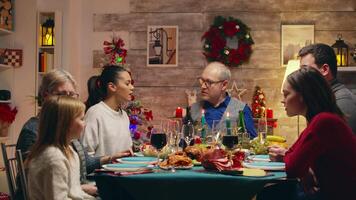 grand-père à le tête de le table tandis que célébrer Noël. famille réunion pour xmax veille. traditionnel de fête Noël dîner dans multigénérationnel famille. profiter Noël repas le banquet dans décoré chambre. gros famille réunion video