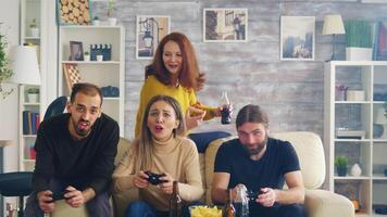 Group of friends trying to beat each other while playing video games sitting on couch using wireless controller. Girl cheering.