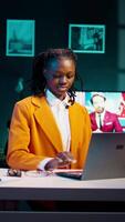 Vertical Video Portrait of african american student putting glasses on and working on english essays at home, reading academic databases for additional resources. Young woman studying at university. Camera B.