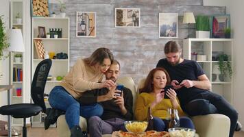 grupp av vänner Sammanträde på soffa använder sig av deras smartphones med pizza och popcorn i främre av de dem. video