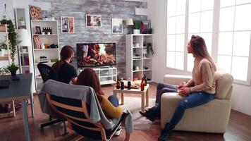 två vuxen män och kvinnor tittar på en TV visa i levande rum. tillbaka se av vänner tittar på tv. video