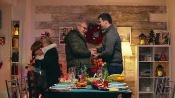 Young man shaking hands with his father in law at christmas celebration with the family. Greeting grandparents, traditional christmas dinner in multigenerational family. People celebrating with festive homemade meal. Holiday spirit christmas eve video