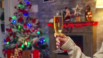 Young woman holding sparkling champagne celebrating christmas with her husband with xmas tree in the background. Christmas tree celebration, new year eve with sparkling wine in cozy home with fireplace. Xmas emotions holiday and family video