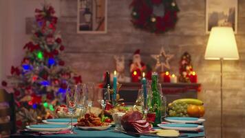 Glasses for champagne on christmas table with delicious traditional food. Xmas celebration in decorated room full of globe decorations and christmas tree with fireplace, big festive dinner meal for large family video