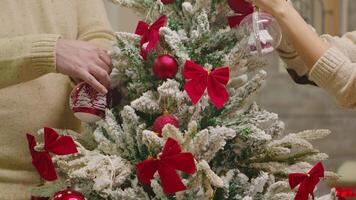 proche en haut de Jeune couple décorer Noël arbre avec rouge globes. décorer magnifique Noël arbre avec verre Balle décorations. épouse et mari dans correspondant à vêtements portion fleuri Accueil avec guirlande lumières video