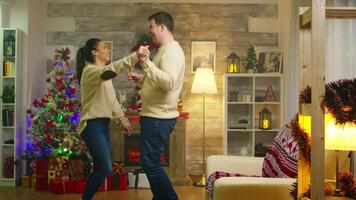 vrolijk jong paar dansen in leven kamer vieren Kerstmis Kerstmis boom in de achtergrond. Kerstmis vakantie samen viering van liefde, pret dans romantisch levensstijl in versierd kamer met haard in achtergrond video