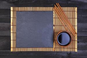 Bamboo mat and soy sauce on dark wooden table. Top view photo