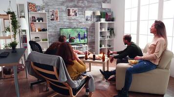 Back view of two girls having a conversation in living room while the boys are watching tv and drinking beer. video