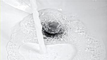 A stream of water pours from the open tap into the sink. On a white background. Filmed on a high-speed camera at 1000 fps. High quality FullHD footage video