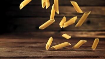 Pasta penne dry falls on the table. On a wooden background. Filmed on a high-speed camera at 1000 fps. High quality FullHD footage video