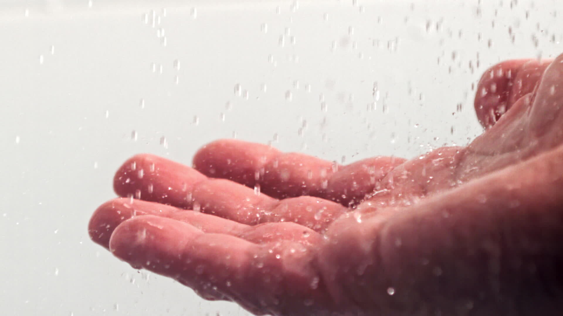 Drops of water pour on a man's hand. On a white background. Filmed on a