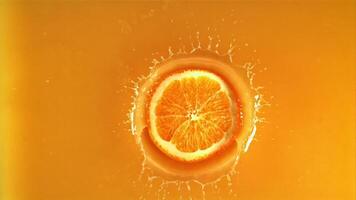 A round piece of fresh orange falls into orange juice with splashes. Top view. Macro background.Filmed is slow motion 1000 fps. video