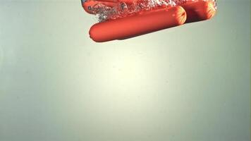 Under the water with air bubbles, sausages fall. On a gray background. Filmed on a high-speed camera at 1000 fps. High quality FullHD footage video