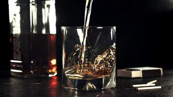 A stream of cognac pours into a glass on the table. On a black background. Filmed on a high-speed camera at 1000 fps. High quality FullHD footage video