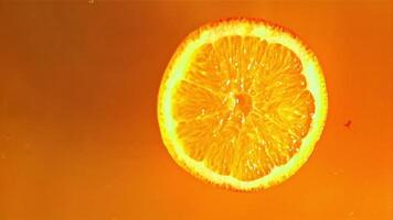 un redondo pedazo de naranja caídas dentro el naranja jugo con salpicaduras macro fondo.filmado en un alta velocidad cámara a 1000 fps. video