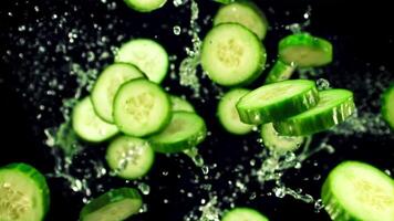 Pieces of fresh cucumbers with splashes of water fly up and rotate in flight. On a black background. Top view. Filmed is slow motion 1000 fps. video