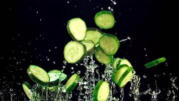 Pieces of fresh cucumber fly up and fall with drops of water. On a black background. Filmed is slow motion 1000 fps. video