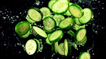 Pieces of fresh cucumber with splashes of water fly up and rotate in flight. On a black background. Top view. Filmed is slow motion 1000 fps. video