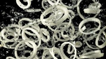 Onion rings with splashes of water fly up and rotate in flight. Top view. On a black background. Filmed on a high-speed camera at 1000 fps. video