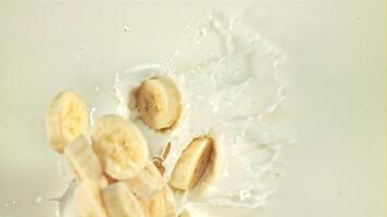 Sliced banana falls into milk with splashes. Top view. On a white background. Filmed is slow motion 1000 fps. video