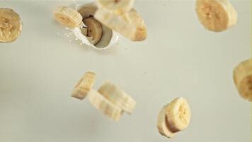 Sliced banana falls into milk with splashes. Top view. On a white background. Filmed is slow motion 1000 fps. video