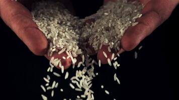 From men's palms pours raw rice. On a black background. Filmed on a high-speed camera at 1000 fps. video