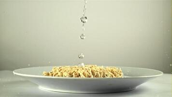 vatten droppar på de torr spaghetti i de tallrik. på en vit bakgrund. filmad på en hög hastighet kamera på 1000 fps. video
