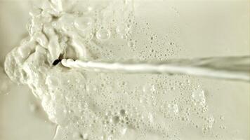 un' ruscello di latte flussi con spruzzi e aria bolle. su un' bianca sfondo. girato su un' alta velocità telecamera a 1000 fps. video