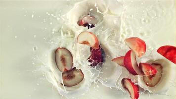 Pieces of red peach fall into the milk. Top view. On a white background. Filmed is slow motion 1000 fps. video