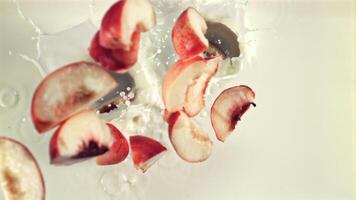 Pieces of red peach fall into the milk. Top view. On a white background. Filmed is slow motion 1000 fps. video