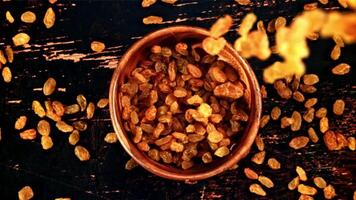 Raisins fall into a wooden bowl on the table. Top view. Against a dark background. Filmed is slow motion 1000 fps. video