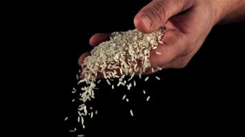 A handful of uncooked rice falls from a man's hand. On a black background. Filmed is slow motion 1000 fps. video